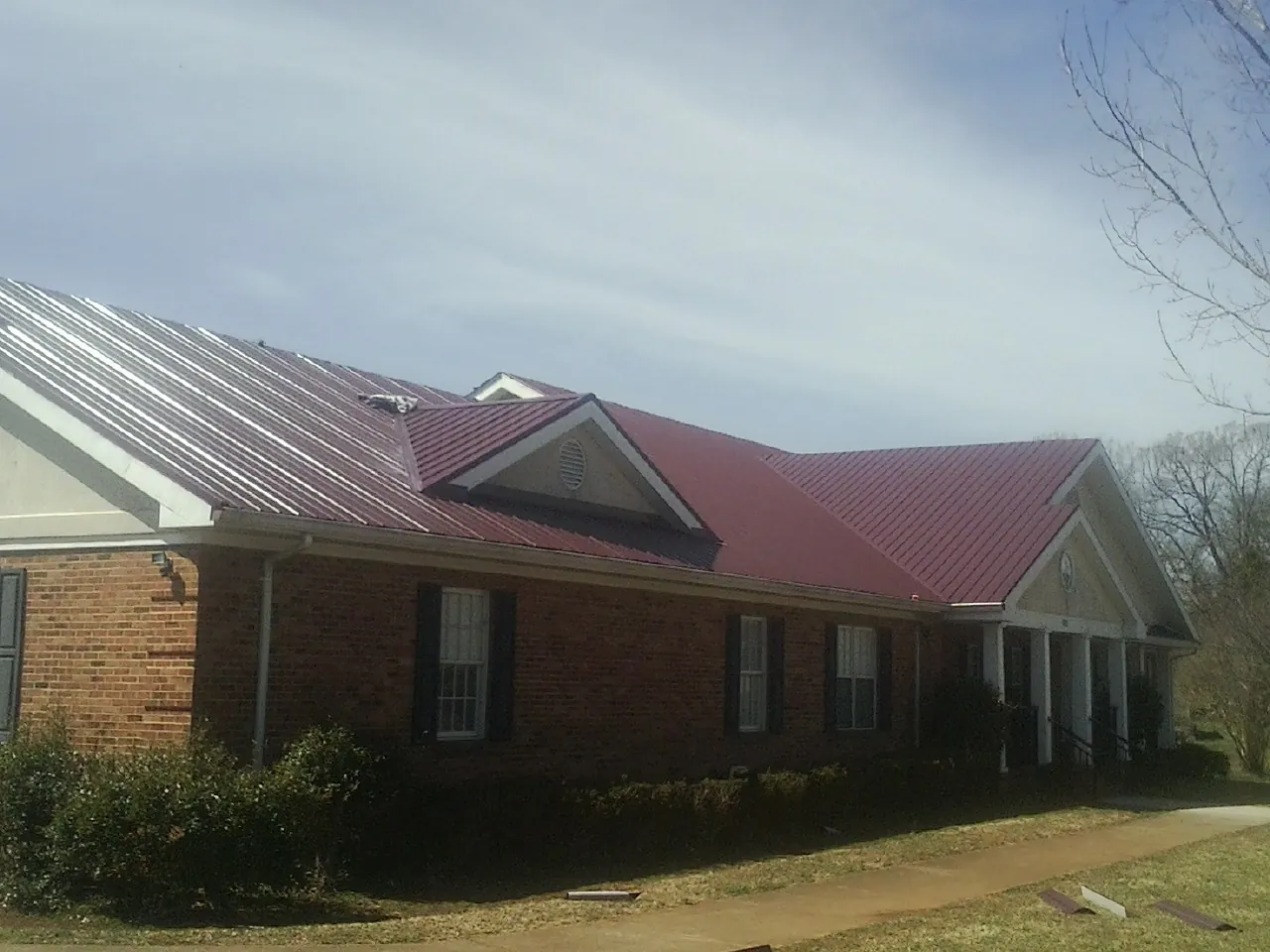 Red metal roof with gabled entries on a long brick building, from a Hail Damage Roof Repair job in Roseburg