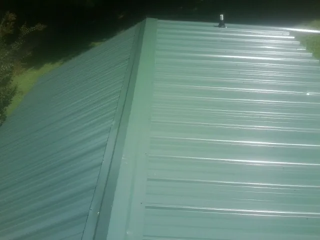 New green metal panels meeting at the ridge of a roof — Flat Roof Repair work by our crew in Roseburg