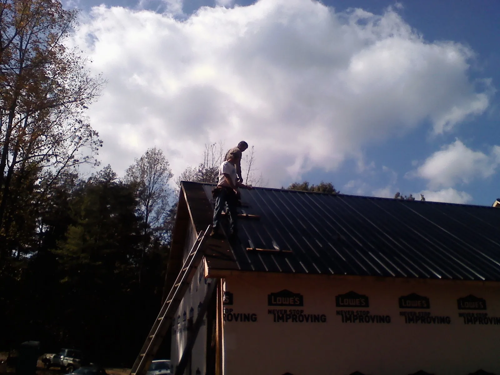 Roofer fastening dark metal panels high against a cloudy sky, from a Roof Inspection job in Roseburg