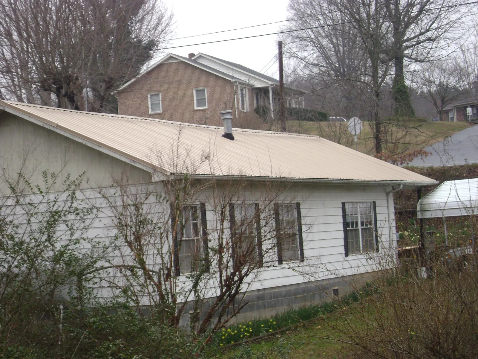 Tan metal roof on a white sided house set into a hillside — Commercial Roofing by Roofing Brothers in Roseburg